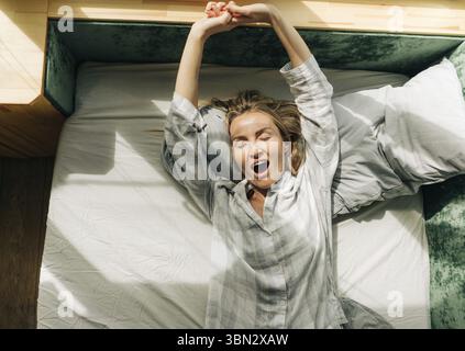 Porträt einer schönen jungen Frau im Pyjama, die im Bett liegt und sich nach dem Aufwachen streckt Stockfoto