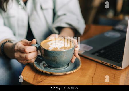 Frauenhände halten eine große Tasse mit Cappuccino am Tisch im Café Stockfoto
