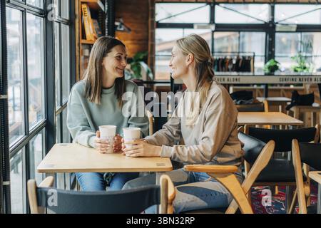 Zwei Freundinnen unterhalten sich und trinken Kaffee, während sie in einem Café sitzen Stockfoto