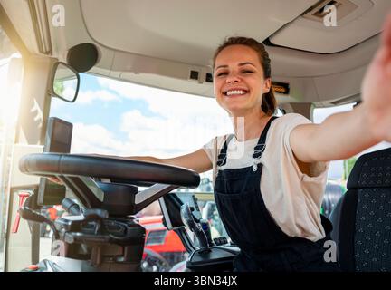 Weibliche Farmarbeiterin, die Selfie in der Traktorkabine auf dem Hof macht. Stockfoto