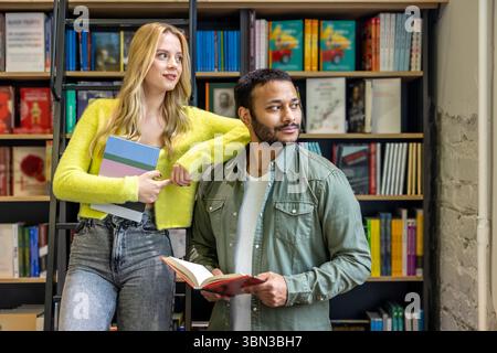 Langhaarige blonde Frau und dunkelhaariger Mann in der Bibliothek Stockfoto