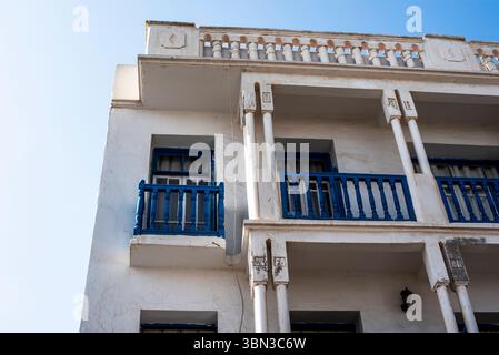 Blau lackierte Holzbalkone an der weißen Fassade eines alten Gebäudes mit langen ruinierten Säulen in den Straßen von Marrakesch Marokko Stockfoto