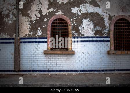 Bogenfenster im alten Hafen von Essaouira mit schmiedeeisernen Gittern und weißen und blauen Azuleias, die durch Zeit und Wetter ruiniert wurden Stockfoto