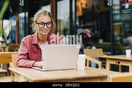 Eine attraktive weiße Frau, die in einem Café sitzt, arbeitet an einem Laptop Stockfoto
