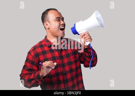Energischer indonesischer Mann im Flanellhemd-Outfit, der Megaphon hält und schrie und stolz den kleinen Finger zeigt, der nach der Wahl in violette Tinte getaucht ist Stockfoto