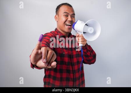 Energischer indonesischer Mann im Flanellhemd-Outfit, der Megaphon hält und schrie und stolz den kleinen Finger zeigt, der nach der Wahl in violette Tinte getaucht ist Stockfoto