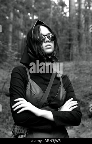 Elegante Frau in grünem Kopftuch und Lederkleid posiert im Wald Stockfoto
