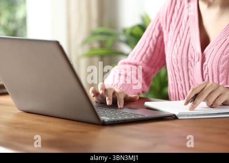 Nahaufnahme Porträt von Frauenhänden, die Laptop und Notizbuch auf Holztisch zu Hause verwenden Stockfoto