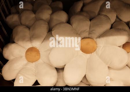 Große weiche Daisy Kissen mit weichen weißen Blüten und gelben Mittelpunkten, gestapelt in einem Display unter warmer Beleuchtung. Nahansicht. Spielzeug zum Verkauf Stockfoto