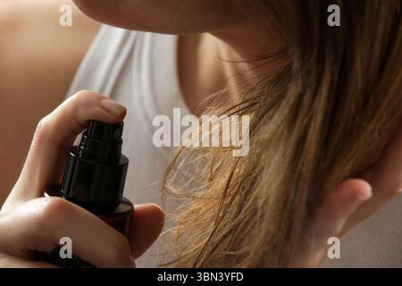 Frau, die Haarpflegespray auf Haarspitzen, gespaltene Haarspitzen, trockenes Haar oder Sonnenschutzkonzept aufträgt Stockfoto