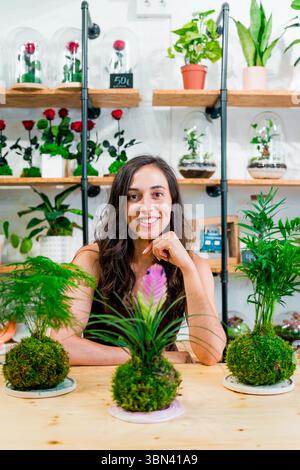 Eine junge Frau posiert mit Kokedamas in einem Blumenladen. Unternehmerin in in ihrem Blumenladen, kleine Geschäftsinhaberin Stockfoto