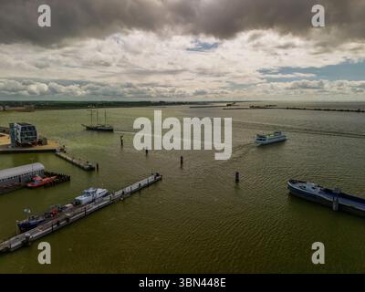Aus der Vogelperspektive auf einen Hafen mit mehreren Booten und Schiffen auf einem großen Gewässer unter dramatischem, bewölktem Himmel, mit einem modernen Gebäude am Wasser und Dock Stockfoto