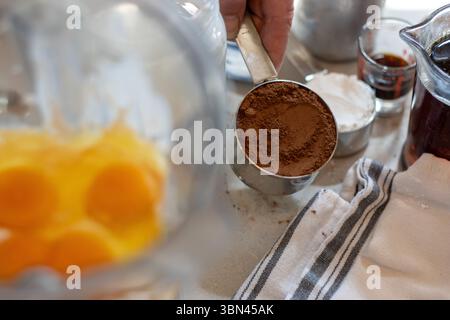 Kakaopulver neben zerbrochenen Eiern im Mixbecher Stockfoto