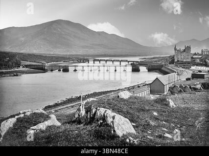 Ein Foto aus dem späten 19. Jahrhundert vom Bahnhof und den Straßen- und Eisenbahnbrücken über den Fluss Ferta in Cahirciveen auf der Iveragh-Halbinsel im County Kerry, Irland. Der extravagant gestaltete Bahnhof Royal Irish Constabulary (RIC) aus den 1870er Jahren wurde im unverwechselbaren Schloss-Stil erbaut, der von seinem Architekten Enoch Trevor Owen bevorzugt wurde und heute ein historisches Zentrum ist. Stockfoto