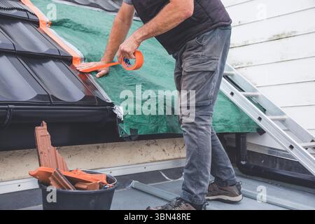 Dachdecker, der nach schlechtem Wetter eine Plane installiert, während er auf Arbeit wartet Stockfoto