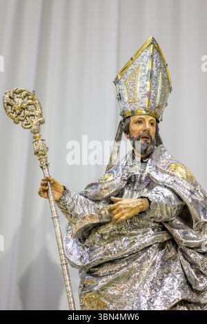 Diese vielfarbige Skulptur des Heiligen Isidor steht in der Kathedrale von Sevilla, mit silbernen Gewändern geschmückt und von Blumen und Kerzen umgeben. Stockfoto