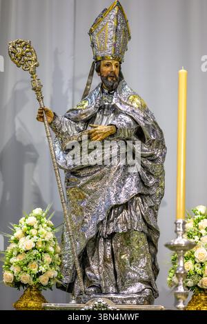 Diese vielfarbige Skulptur des Heiligen Isidor steht in der Kathedrale von Sevilla, mit silbernen Gewändern geschmückt und von Blumen und Kerzen umgeben. Stockfoto