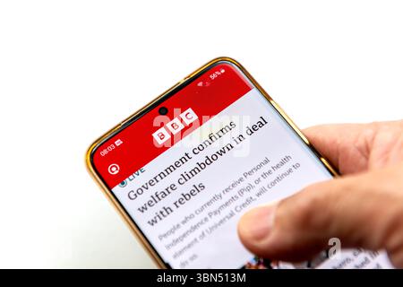 London. UK- 06.27.2025. Eine Person, die ein Smartphone hält, während die Anwendung BBC News auf dem Bildschirm isoliert auf weiß angezeigt wird. Stockfoto