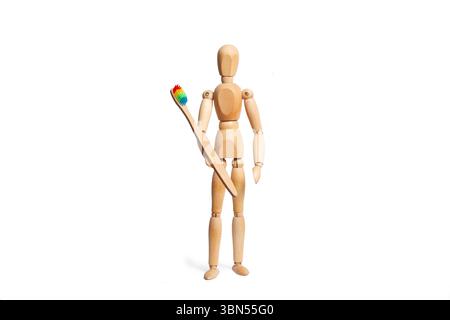 Eine hölzerne Spielzeugpuppe, die eine Zahnbürste in der Hand auf weißem Hintergrund hält Stockfoto