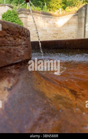 Mineralwasser Trinkwasserquelle Trinkwasser strömt aus dem Wasserhahn auf der Straße. Ein alter rostiger Wasserhahn, aus dem Wasser in einen Wassertank fließt Stockfoto