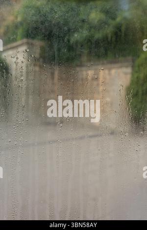 Nahaufnahme eines dampfenden Fensters mit Wassertropfen. Wassertropfen auf das beschlagene Glas. Dreckiges Glas mit Tropfen nach Regen Stockfoto