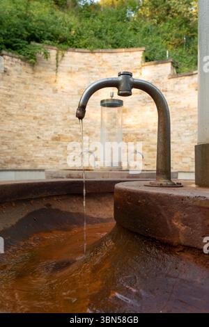 Mineralische Trinkwasserquelle. Trinkwasser strömt aus dem Wasserhahn auf der Straße. Ein alter rostiger Wasserhahn, aus dem Wasser in einen Wassertank fließt Stockfoto