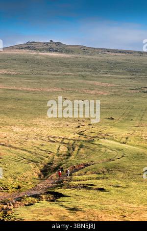 Der Fernblick von zwei Wanderer auf der rauen Strecke, die zum Roughtor Rough Tor auf dem wilden windgepeitschten Bodmin Moor in Cornwall in Großbritannien führt. Stockfoto
