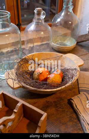 Kleine Kürbisse in Holzschale auf rustikalem Holztisch mit Glasflaschen und rustikaler Holzkiste in Heimschuh, Steiermark Stockfoto