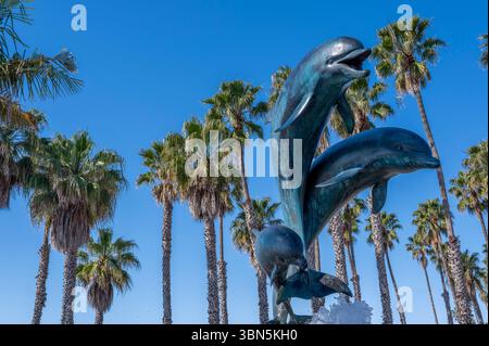 Skulpturen von drei Delfinen und majestätischen Palmen erheben sich vor einem makellosen azurblauen Himmel im amerikanischen Westen Stockfoto