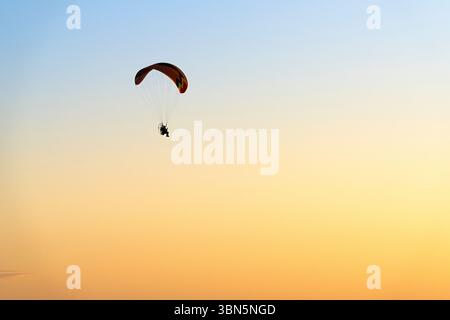 Einsame Gleitschirmflieger fliegen über einen leuchtend orange-gelben Sonnenaufgangshimmel über Alice Springs, Australien. Horizontales Bild mit reichlich Kopierraum. Stockfoto