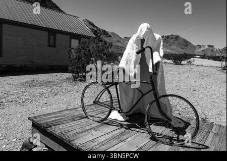 Eine geisterhafte Figur in weiß hängt mit einem Vintage-Fahrrad in der Wüstenlandschaft von feerie in Rhyolite, Nevada Stockfoto