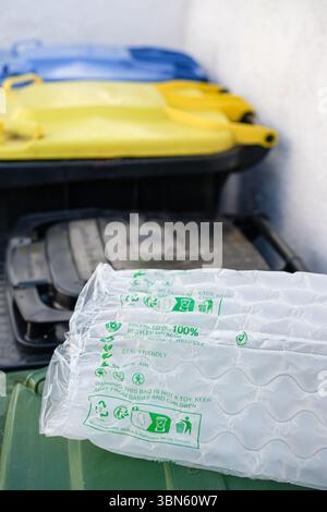 Kunststoff-Luftkissen aus recyceltem Material mit grünen umweltfreundlichen Symbolen und Text. Abfallbehälter oder Abfallbehälter daneben. Stockfoto