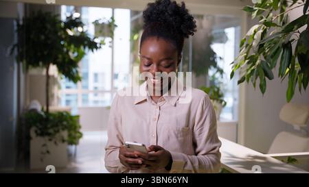 Afroamerikanische Geschäftsfrau lächelndes ethnisches Mädchen Geschäftsfrau mit Handy-Gadget im Büro fröhliche fröhliche weibliche Studentinnen-Arbeitgeber-Managerin Stockfoto