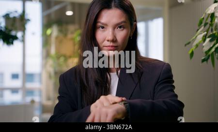 Asiatische ernsthafte Geschäftsfrau Blick auf Kamera Geschäftsfrau zeigt Armbanduhr warten Meeting Check Time Eile Deadline Pünktlichkeit im Büro Chinesisch Stockfoto