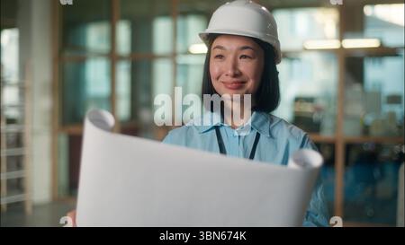 Asiatische Frau Ingenieur Erbauer in Sicherheit Schutzhelm lächelnd chinesisches koreanisches Mädchen japanisches Mädchen Industriearchitektur Bauunternehmer Inspektor, der sich einen Plan ansieht Stockfoto