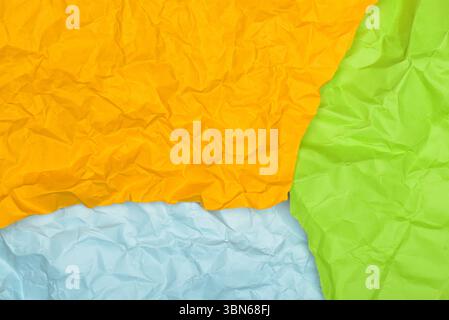 Ein lebendiges Bild mit zerknitterten Blättern aus gelbem, hellblauem und grünem Papier, die in einer abstrakten Komposition angeordnet sind. Stockfoto