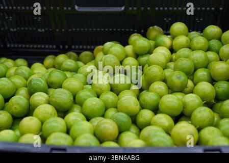 Eine Nahaufnahme einer leuchtenden schwarzen Kunststoffkiste mit zahlreichen leuchtenden grünen Limetten. Stockfoto