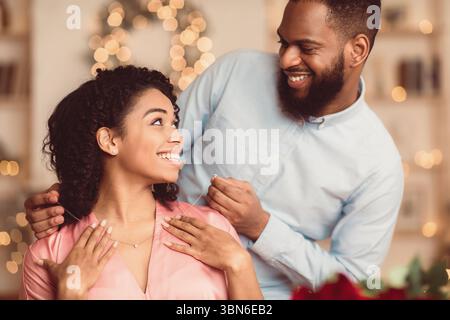 Junger schwarzer Kerl trägt Halskette auf seiner lächelnden Frau Stockfoto