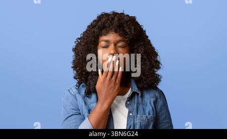 afroamerikanische Frau, die auf gelb gähnt und den Mund mit der Hand bedeckt Stockfoto