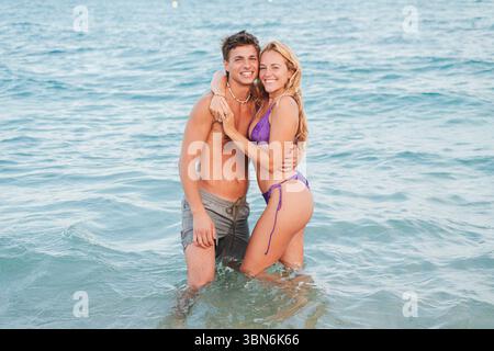 Ein fröhliches Paar teilt sich eine warme Umarmung im erfrischenden Meer, umgeben von der Schönheit des Strandes. Ihr Lachen erfüllt die Luft, während sie kreieren Stockfoto