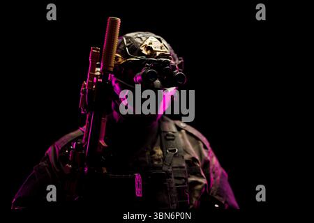 Ein taktischer Soldat, ausgestattet mit Nachtsichtbrille und Waffen, beleuchtet mit lebendigem Licht. Zeigt Kriegsführung, Technologie und Bereitschaft. Stockfoto