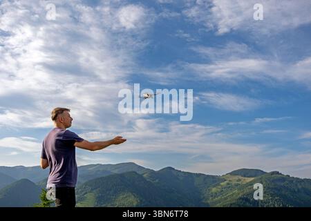 Ein Mann, der Drohnen über die Berglandschaft fliegt. Ein Mann betreibt eine Drohne in einem malerischen Berggebiet unter einem hellblauen Himmel, um die Natur aus der Luft zu betrachten Stockfoto