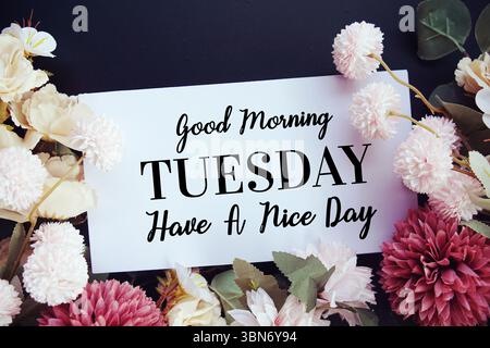 Guten Morgen Dienstag, hab einen schönen Tag Text mit Blumendekorationen auf schwarzem Hintergrund Stockfoto