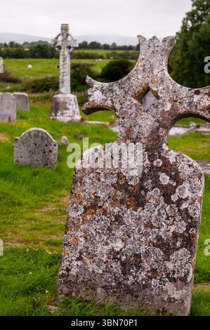 Ein Friedhof mit einem Kreuzgrabstein in der Mitte. Der Grabstein ist von Gras umgeben und im Hintergrund befinden sich weitere Grabsteine Stockfoto