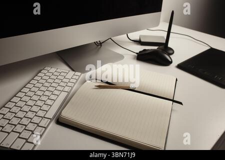 Moderner Arbeitsbereich mit Tastatur, schwarzem Notebook, Bleistift, Grafiktablett und Stiften auf weißem Schreibtisch. Draufsicht für kreatives Projekt. Stockfoto