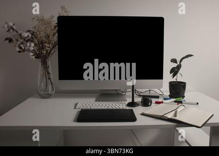 Minimalistischer Home Office-Arbeitsplatz mit Desktop-Computer, Tastatur, Notebook, Stifttablett, getrockneten Blumen und einer Pflanze auf einem sauberen weißen Schreibtisch. Arbeiten Sie zu Hause Stockfoto