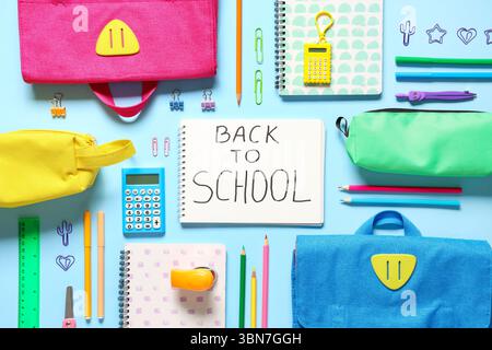 Schulrucksäcke, Notizbuch mit Text ZURÜCK ZUR SCHULE und verschiedene Schreibwaren auf blauem Hintergrund Stockfoto