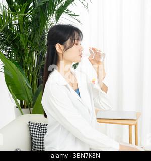 Eine junge Frau, die Wasser aus einer Tasse gießt und trinkt. Stockfoto