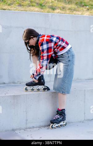 Eine junge Frau, die ihre Inline-Skates in einem urbanen Park fesselt und sich auf eine aufregende Skating-Session voller Energie und Spaß vorbereitet Stockfoto