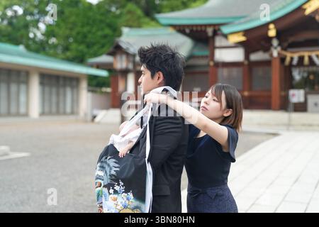 Im Juni 2025 befindet sich ein junges japanisches Paar Anfang 20 in einem Shinto-Schrein in Aichi. Die Mutter hilft dem Vater sanft, seinen Monat zu kleiden Stockfoto